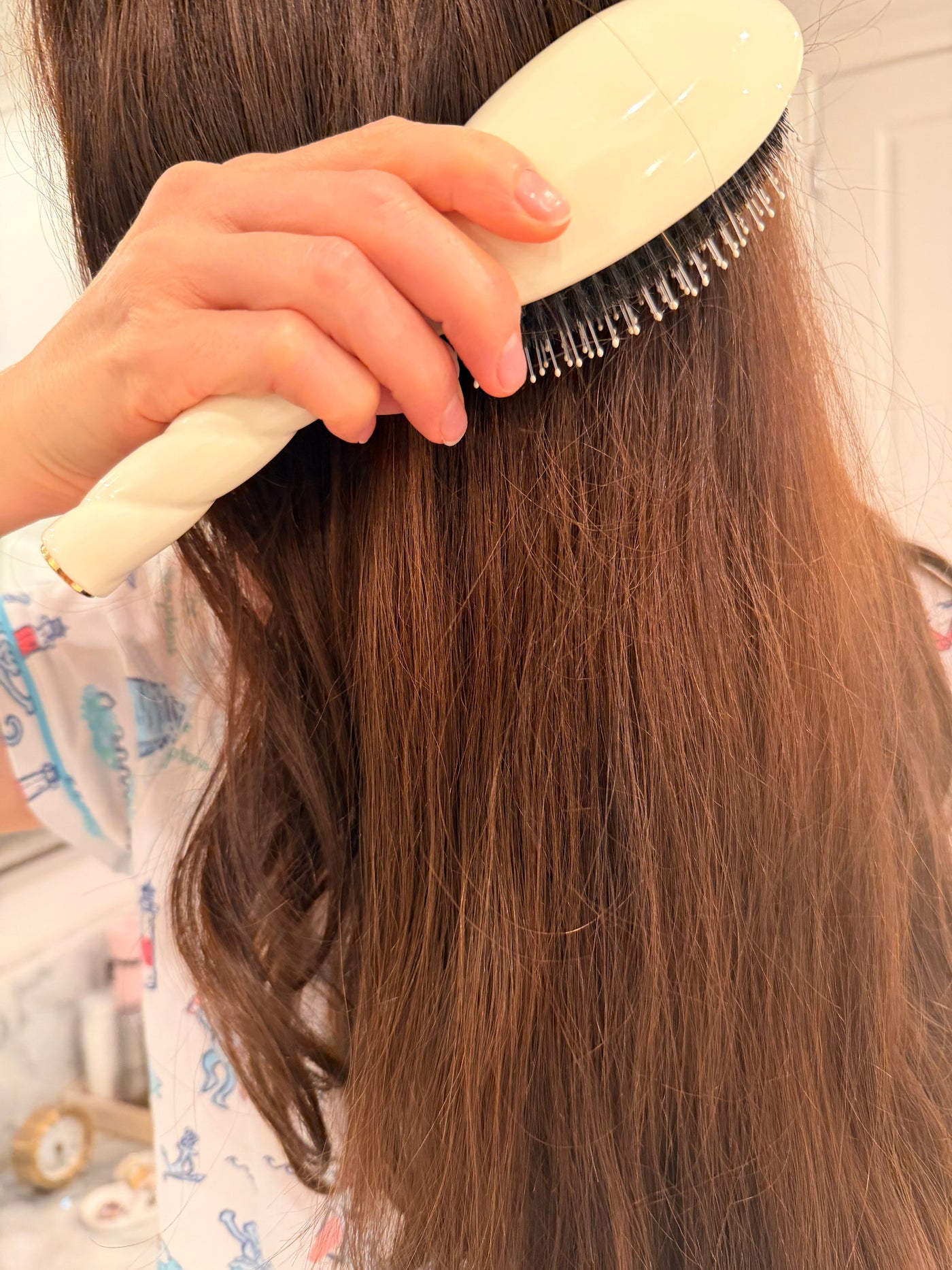 Brushing long brown hair with a cream-handled paddle brush