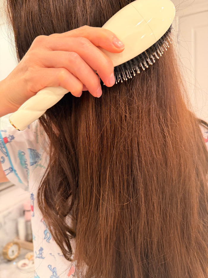 Brushing long brown hair with a cream-handled paddle brush